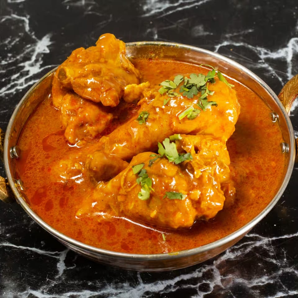 Zaika's Indian chicken curry with drumsticks and cilantro in a metal bowl on a marble surface.
