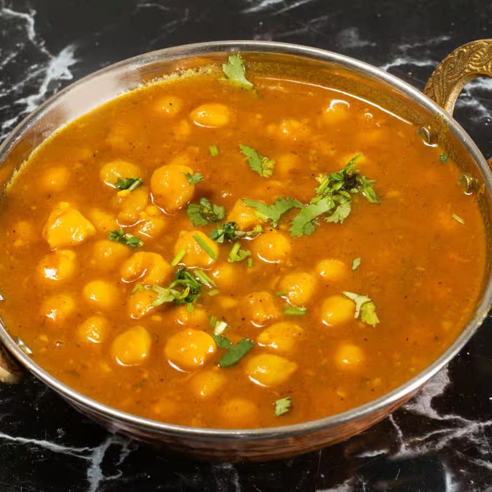 Zaika's chana masala, a chickpea curry, garnished with fresh cilantro in a copper bowl.