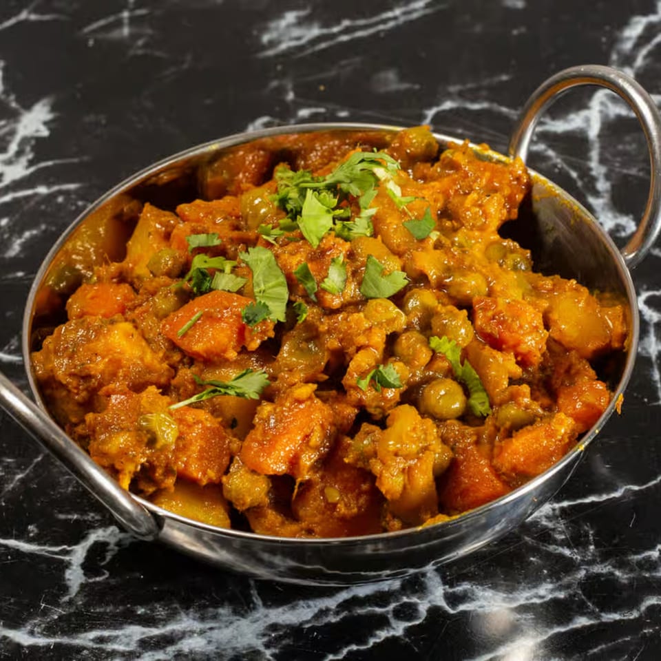 Zaika's Indian vegetable curry, garnished with fresh cilantro, in a traditional metal serving bowl.