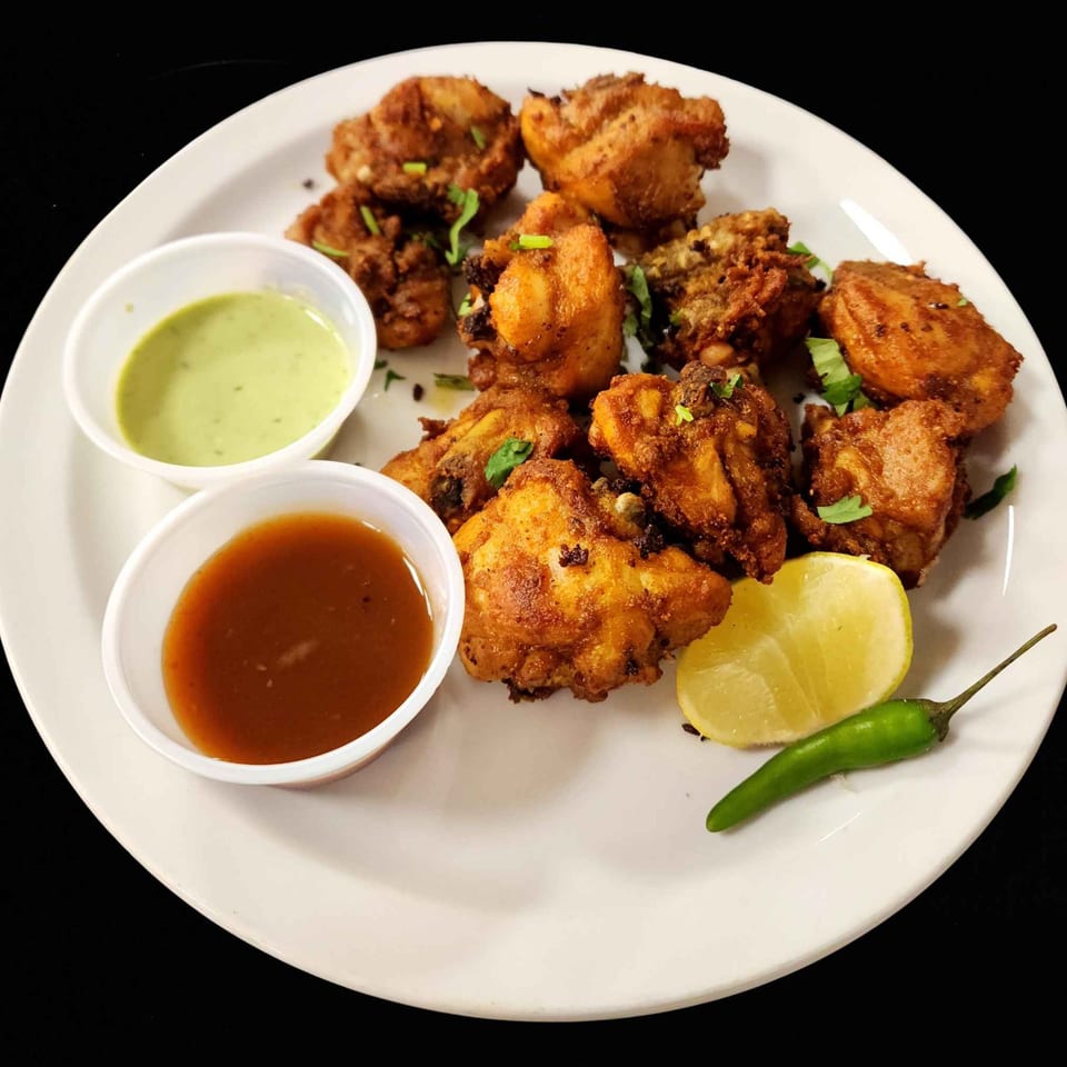 Zaika's Indian fried chicken with green and brown sauces, a lemon wedge, and a green chili.