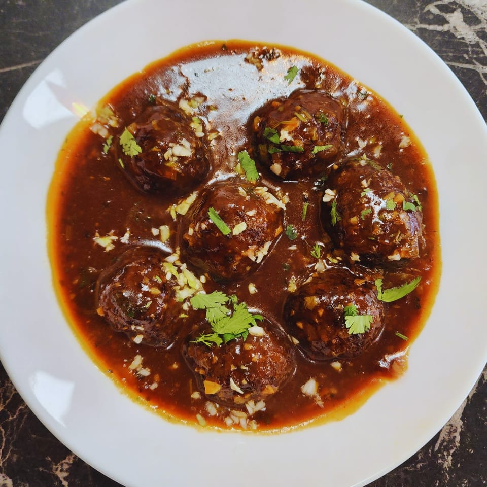 Zaika's Indian dish features dark brown meatballs in a rich sauce, garnished with chopped garlic and cilantro.