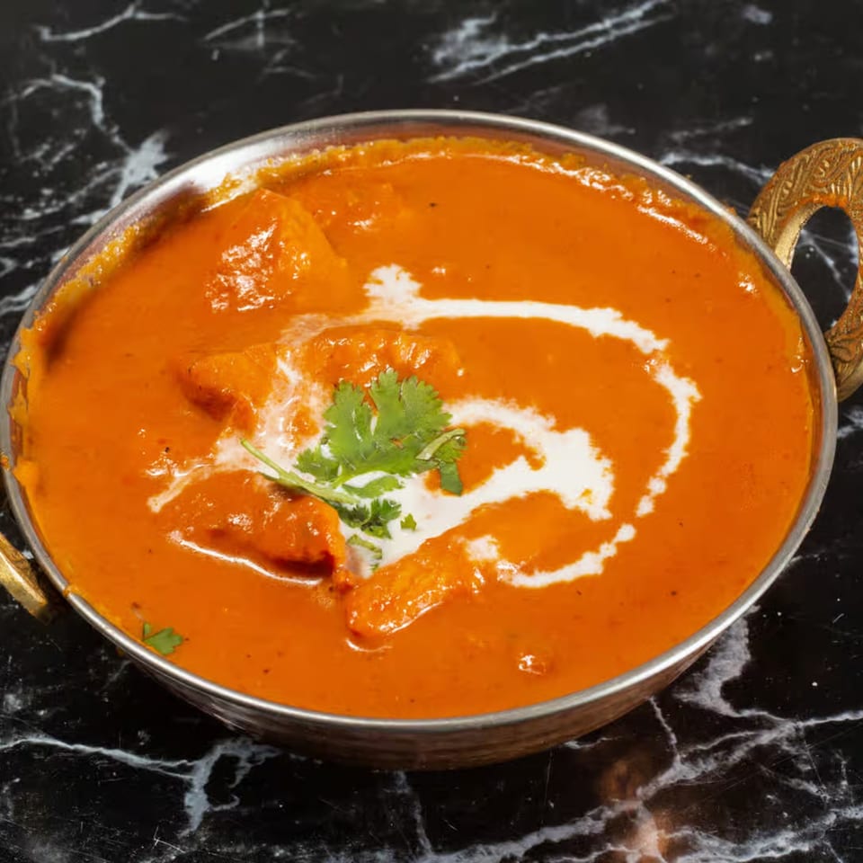 Zaika's Indian butter chicken in a metal bowl, garnished with cream swirls and cilantro.